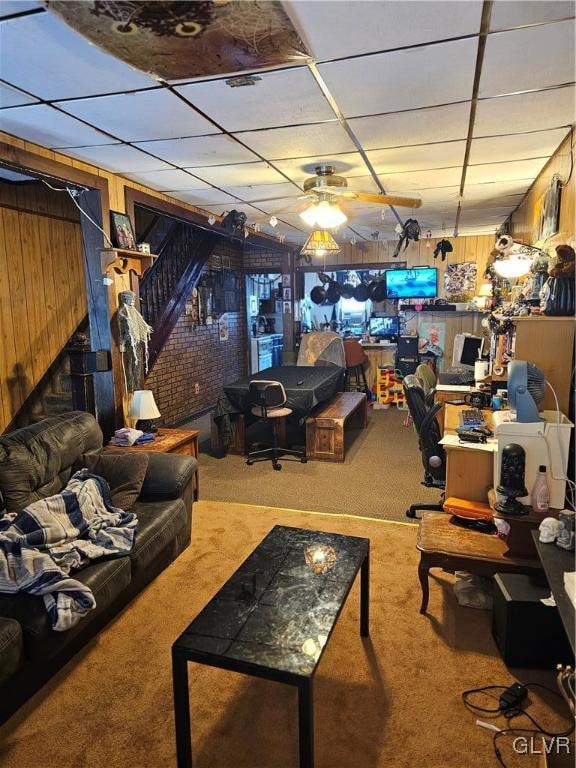 interior space with carpet flooring, wood walls, ceiling fan, and a drop ceiling