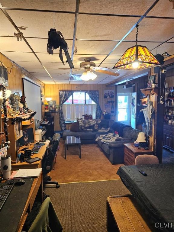 carpeted office featuring ceiling fan and wooden walls