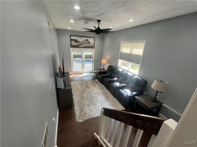 living room with ceiling fan, a textured ceiling, and dark wood-type flooring