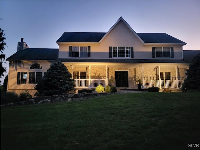 back house at dusk with a porch and a lawn