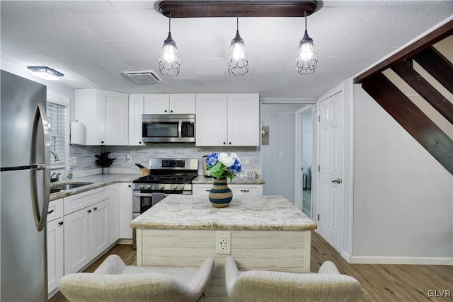 kitchen featuring light hardwood / wood-style floors, decorative light fixtures, stainless steel appliances, and a kitchen island