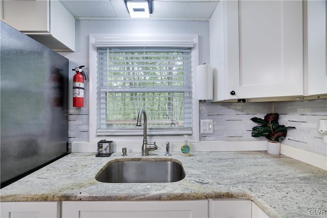 kitchen with white cabinets, light stone counters, decorative backsplash, and sink