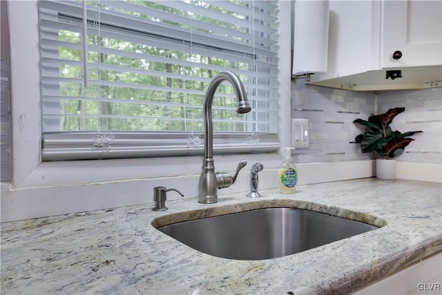 details with tasteful backsplash, light stone counters, sink, and white cabinets