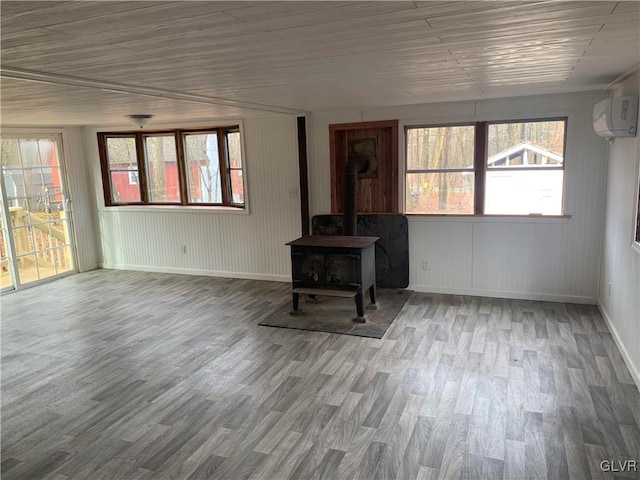 unfurnished living room featuring a wood stove, an AC wall unit, and hardwood / wood-style flooring