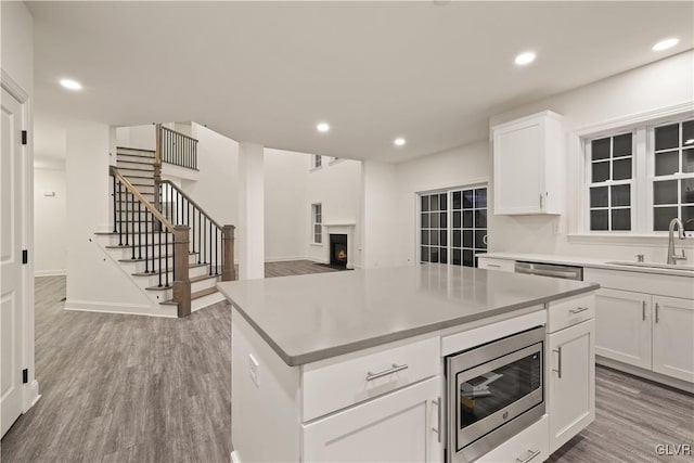 kitchen with a center island, light hardwood / wood-style flooring, white cabinetry, sink, and stainless steel microwave