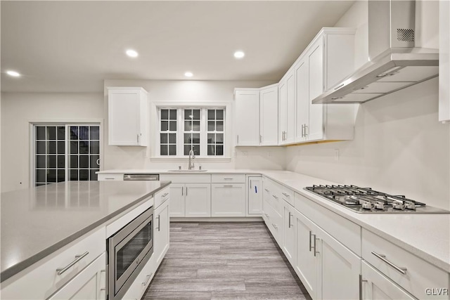 kitchen with wall chimney range hood, appliances with stainless steel finishes, and white cabinetry