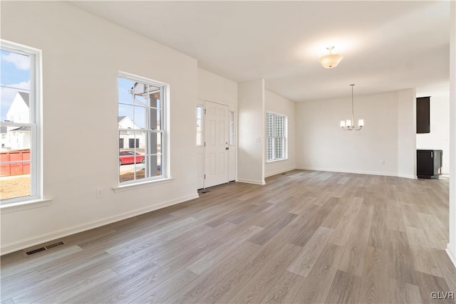 unfurnished living room with an inviting chandelier, plenty of natural light, and light hardwood / wood-style floors