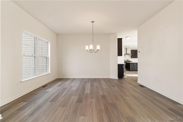 unfurnished dining area with a healthy amount of sunlight, an inviting chandelier, and hardwood / wood-style floors