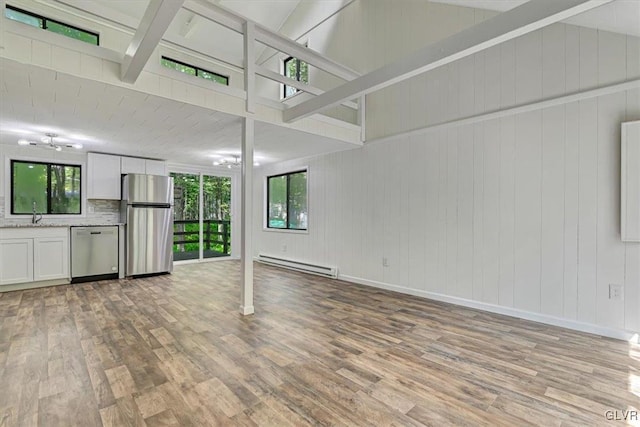 unfurnished living room with wooden walls, light hardwood / wood-style floors, plenty of natural light, and a baseboard heating unit