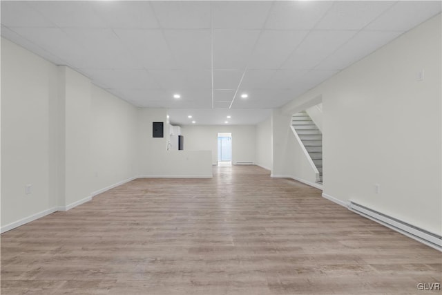 basement featuring a baseboard heating unit, light hardwood / wood-style flooring, and a paneled ceiling