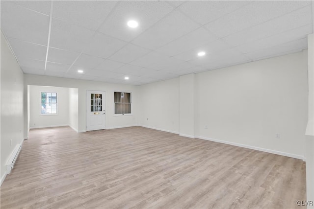 basement with a drop ceiling, a baseboard radiator, and light hardwood / wood-style floors