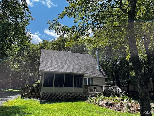 view of front of house featuring roof with shingles, a deck, a front yard, and a sunroom