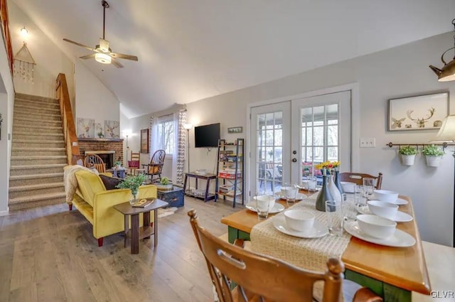 dining area featuring wood finished floors, high vaulted ceiling, a fireplace, stairs, and french doors