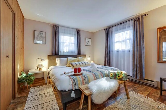 bedroom with multiple windows, a baseboard heating unit, and wood finished floors