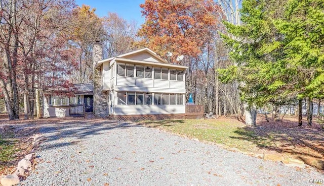 view of front of property featuring driveway, a front yard, a chimney, and a sunroom