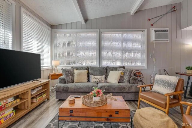 living room with a textured ceiling, light hardwood / wood-style floors, a wall unit AC, wooden walls, and vaulted ceiling with beams