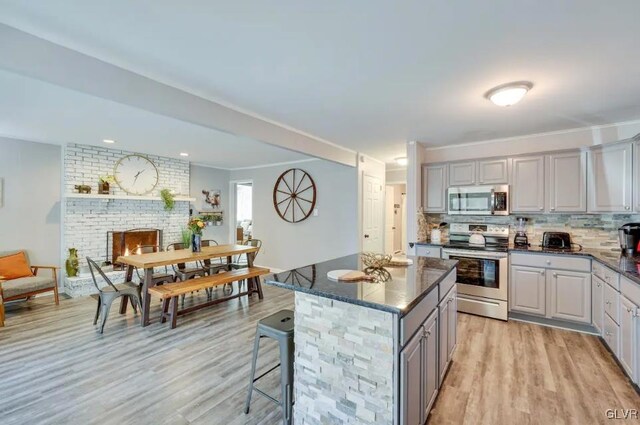 kitchen featuring gray cabinetry, a center island, a fireplace, stainless steel appliances, and light hardwood / wood-style floors