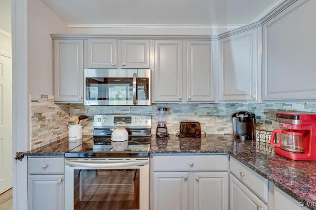 kitchen with dark stone countertops, stainless steel appliances, and backsplash