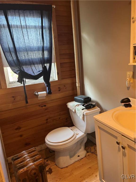 half bath with vanity, wooden walls, toilet, and wood finished floors