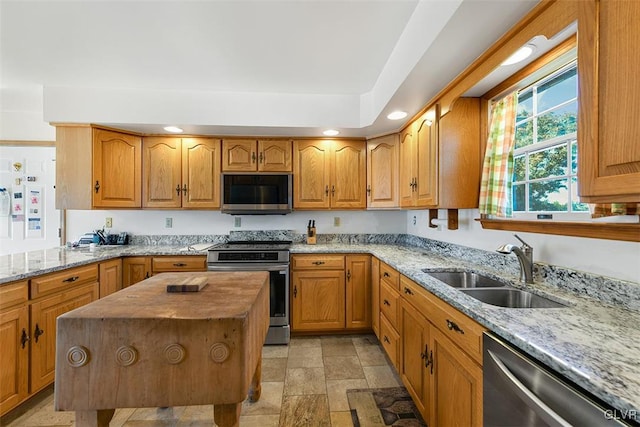 kitchen featuring appliances with stainless steel finishes, a kitchen island, sink, and light stone countertops