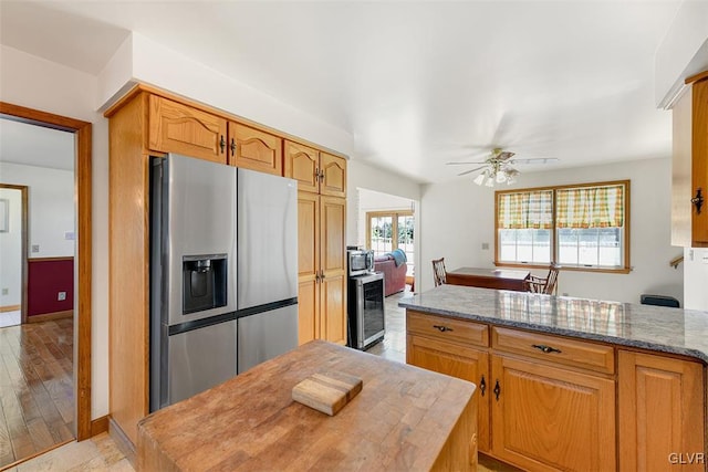 kitchen featuring ceiling fan, light stone counters, light wood-type flooring, and stainless steel refrigerator with ice dispenser