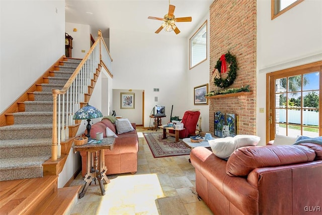 living room with a fireplace, ceiling fan, and a high ceiling