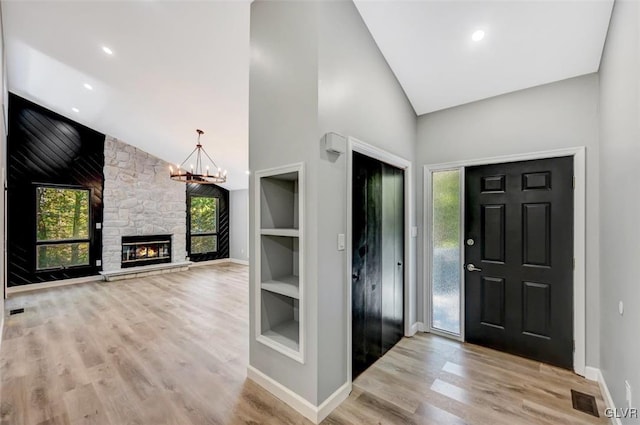 foyer entrance with a stone fireplace, light hardwood / wood-style flooring, a chandelier, and a healthy amount of sunlight