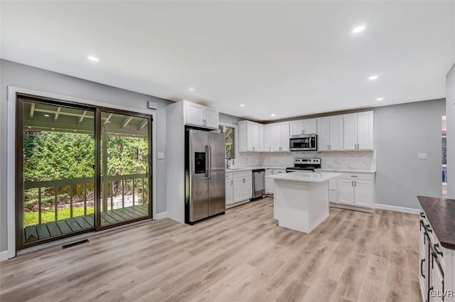 kitchen with light wood-type flooring, white cabinetry, backsplash, a kitchen island, and appliances with stainless steel finishes