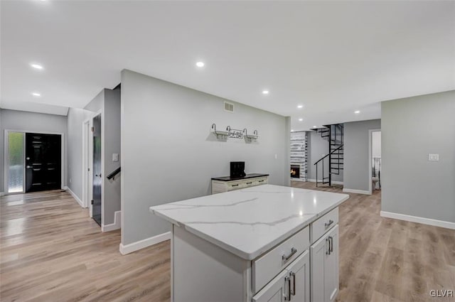 kitchen featuring a kitchen island, light stone countertops, white cabinets, and light hardwood / wood-style floors