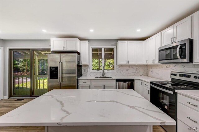 kitchen with appliances with stainless steel finishes, hardwood / wood-style floors, light stone counters, and a kitchen island