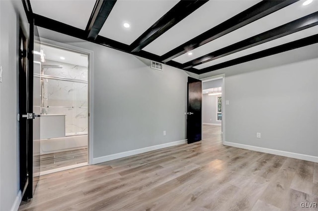 empty room featuring light wood-type flooring and beamed ceiling