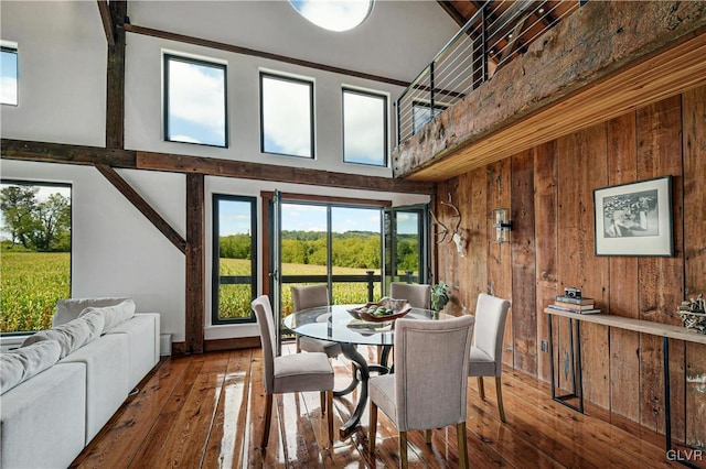 dining area with dark wood-type flooring, wood walls, and a high ceiling