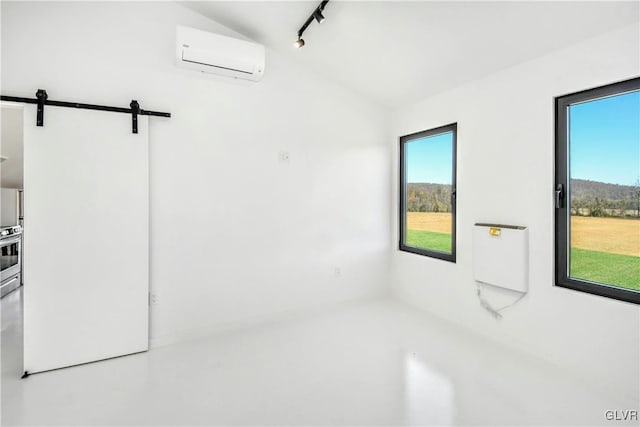 unfurnished room with track lighting, a wall unit AC, a barn door, and concrete floors