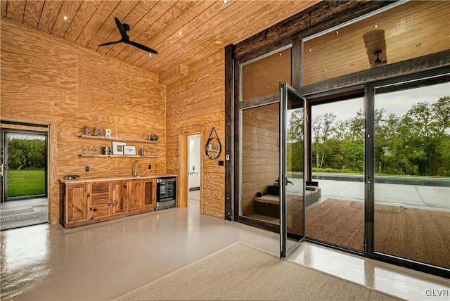 doorway to outside featuring wood walls, concrete floors, sink, high vaulted ceiling, and ceiling fan