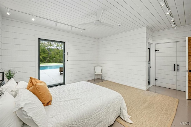 bedroom with wood walls, ceiling fan, rail lighting, and access to outside