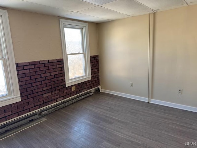 spare room with dark hardwood / wood-style flooring, a drop ceiling, and brick wall