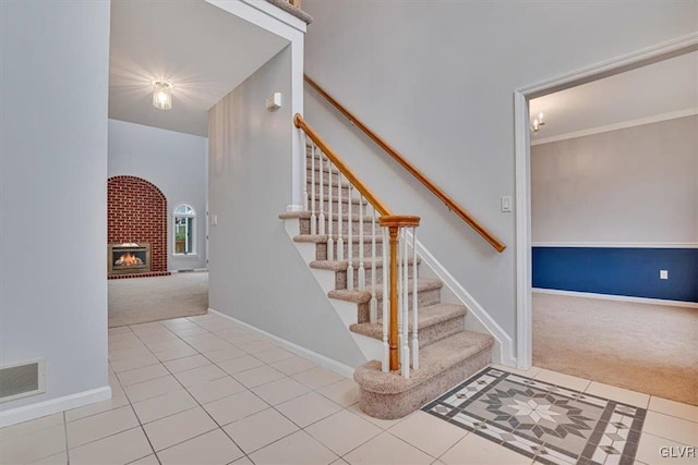 staircase featuring carpet floors, crown molding, and a brick fireplace