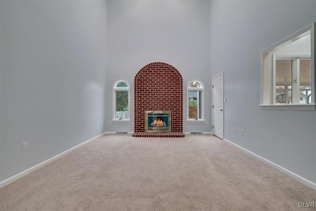 unfurnished living room with light carpet, a high ceiling, and a brick fireplace