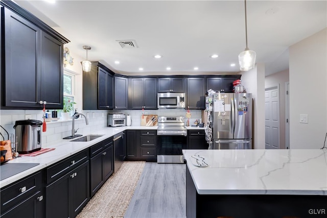 kitchen with appliances with stainless steel finishes, sink, backsplash, decorative light fixtures, and light hardwood / wood-style flooring