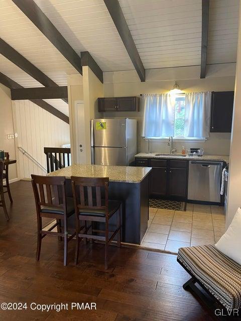 kitchen featuring sink, a center island, stainless steel appliances, beamed ceiling, and a kitchen bar