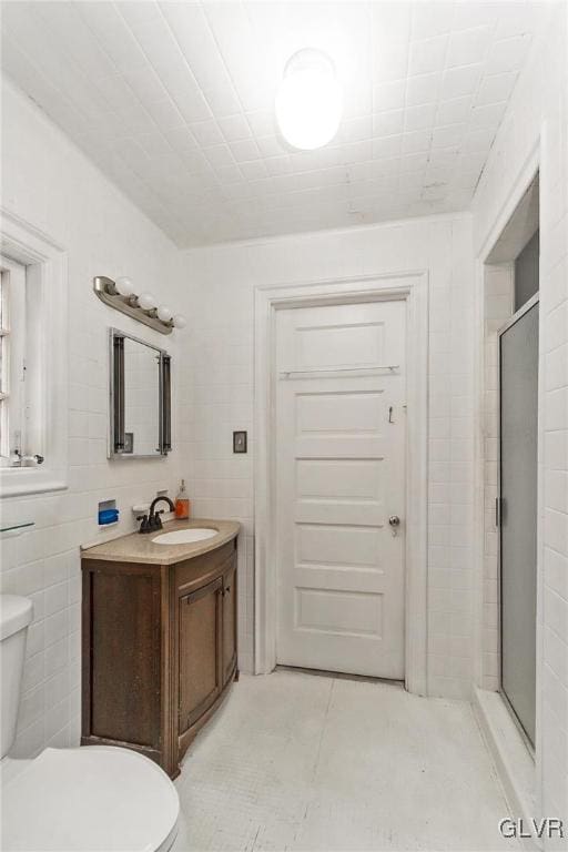 bathroom featuring vanity, tile walls, toilet, and a shower with door