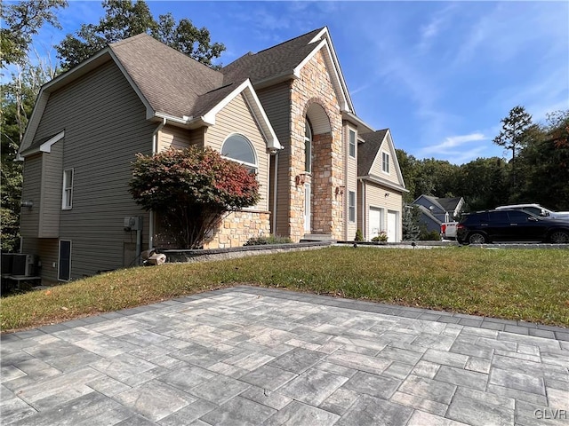 view of side of property with a lawn, a garage, and central AC