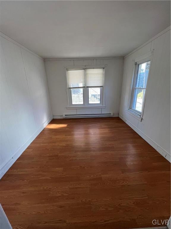 unfurnished room featuring a baseboard heating unit, a healthy amount of sunlight, and dark hardwood / wood-style flooring