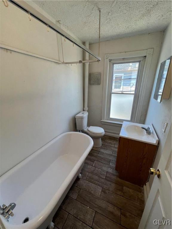 bathroom featuring vanity, a textured ceiling, toilet, hardwood / wood-style flooring, and a washtub