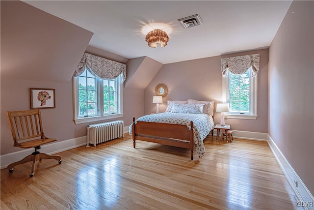 bedroom with light hardwood / wood-style floors, lofted ceiling, and radiator heating unit