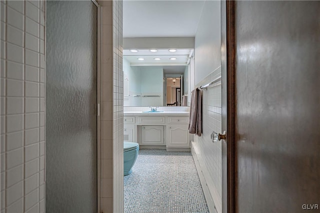 bathroom with vanity, toilet, tile walls, and a shower with shower door