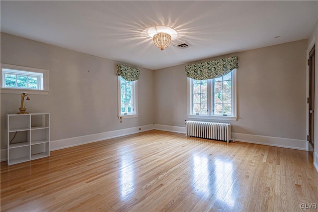 unfurnished room featuring a healthy amount of sunlight, radiator heating unit, and light wood-type flooring