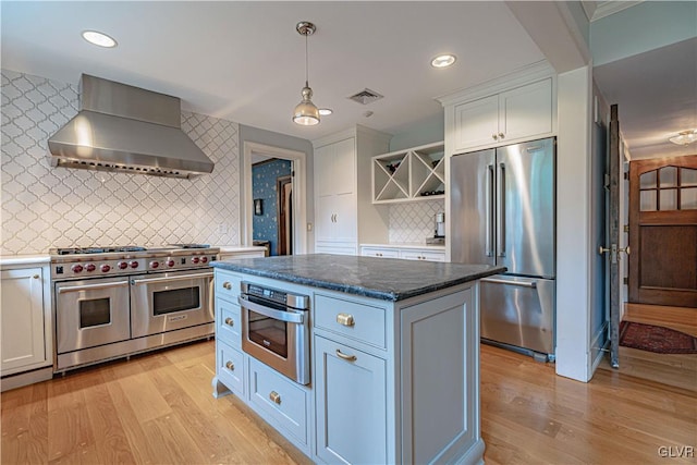 kitchen with decorative backsplash, white cabinetry, light hardwood / wood-style floors, wall chimney exhaust hood, and high quality appliances