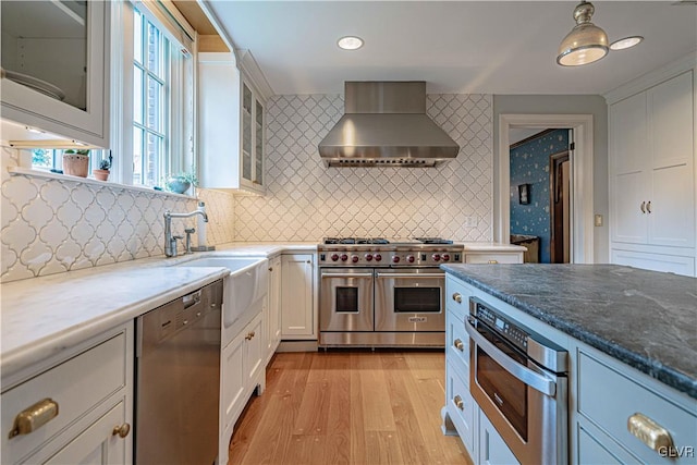 kitchen with white cabinets, wall chimney range hood, stainless steel appliances, and light hardwood / wood-style floors