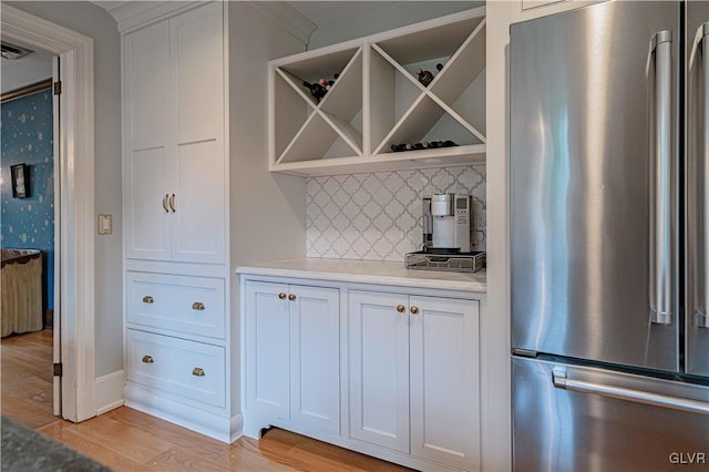 interior space featuring backsplash, ornamental molding, light wood-type flooring, white cabinetry, and stainless steel refrigerator